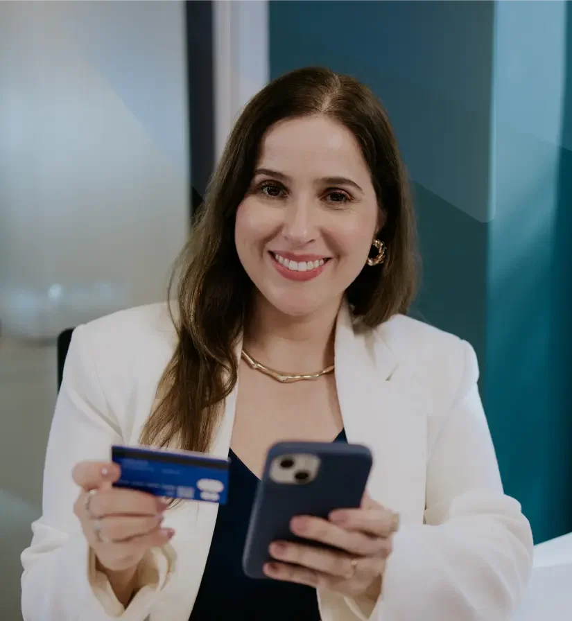 Mulher sorrindo segurando um cartão corporativo e um celular